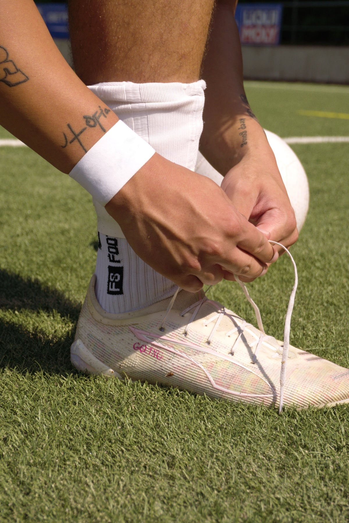 Nahaufnahme eines Spielers, der die Schnürsenkel eines Fußballschuhs bindet. Er trägt das schlichte, unbedruckte weiße Ligora-Fussball-tape von Balora am Handgelenk. 